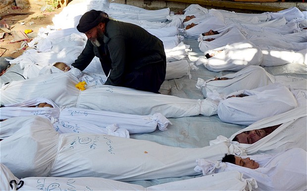 A man cradles the body of a dead child amongst the bodies of dozens of others in Damascus 